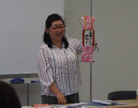 講師の京免 栄美子先生がピンクの掛け軸を参加者に見せながら話をしている写真
