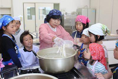 大きな鍋にうどんを入れている大西さんを周りで子供たちが見ている写真