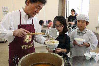 子供たちがうどんが入った器を持って大人の方につゆをかけてもらっている写真