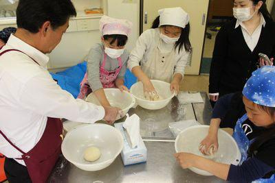 小麦粉を一塊にしている子供3人とボールを持って手伝っている大人の写真