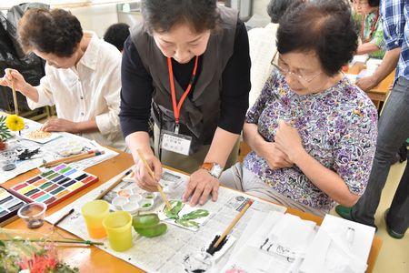 講師の藤田 正子さんが受講生の女性に色塗りのアドバイスをし受講生の女性が真剣にその様子を見ている写真