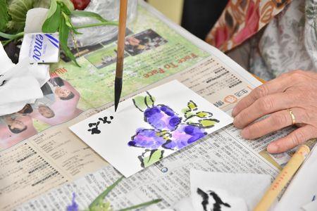 紫色の花を描いたはがきに文字を書いている受講生の写真