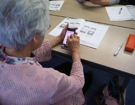 白髪の女性がスマートフォンの説明書を見ながらスマホを触っている写真