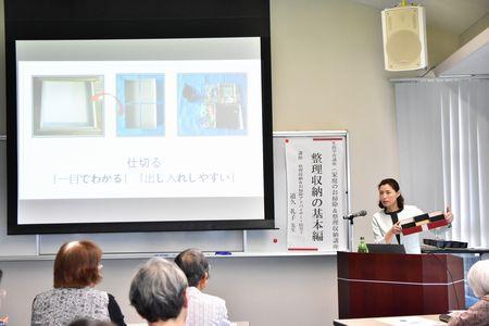 左にはスクリーンが写っていて、右に立った道久 礼子さんが箱を持って話をしている写真