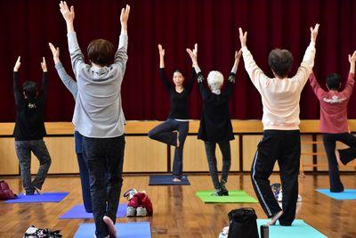 講師の宇賀 花栄さんを見ながら両手を上にあげ、右足の裏を左足に付け左足でバランスを取りながら立っている参加者たちの写真