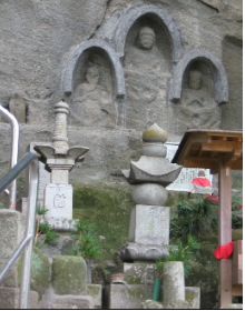石壁に作られた3体の仏像がある前に2体の灯篭が立っている写真