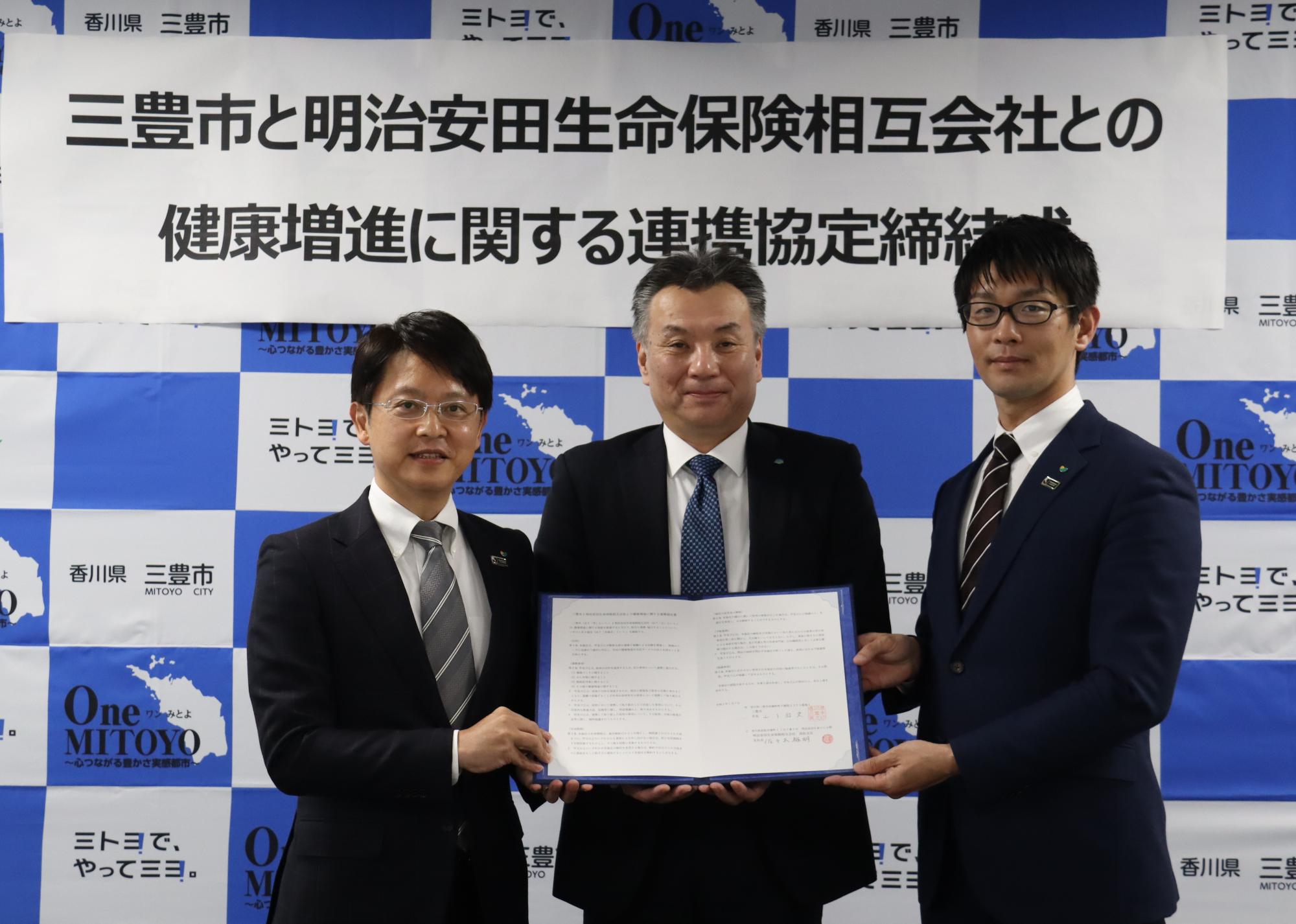 協定書を持つ（左から）明治安田生命相互会社の佐々木高松支店長、山下市長、光岡観音寺営業所長